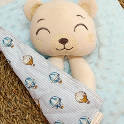 Peluche de urso bege com manta azul e pano riscado com estampado de balões.