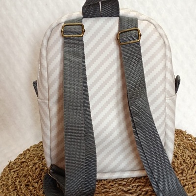 mochila pequena cinza claro com alças cinza escuro sobre superfície de fibras entrelaçadas