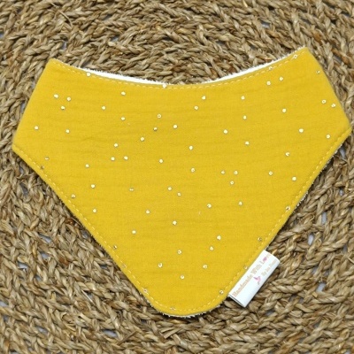 Babete triangular amarelo com pontos brilhantes sobre tapete de fibras naturais entrelaçadas