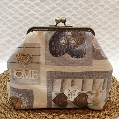 Carteira cremosa bege com estampado de corações e palavras, fecho metálico dourado, sobre base trançada de palha.