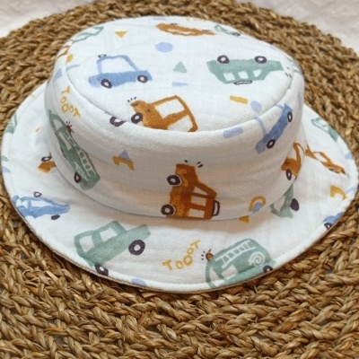 Chapéu de tecido branco com estampado de carrinhos coloridos e texto Tooot sobre tapete trançado castanho.