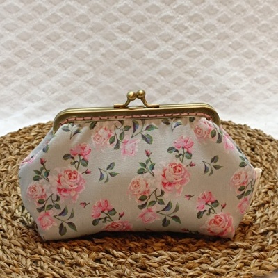 Carteira pequena cinza com flores cor-de-rosa e fecho dourado sobre base trançada