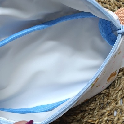 Interior de mala pequena com fecho azul e tecido estampado colorido sobre superfície trançada.