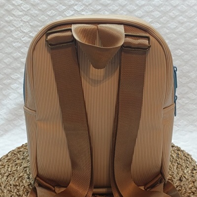 Mochila pequena bege com riscas brancas, alças castanhas largas ajustáveis, sobre base trançada castanha