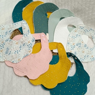 Babetes para bebé em várias cores e padrões florais com detalhes em dourado.