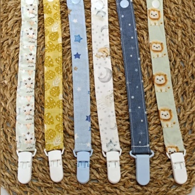 Seis porta-chupetas em tecido com diferentes padrões sobre base trançada