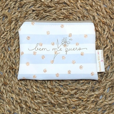 Carteira pequena azul claro, branco e castanho com texto bem me quero e flor, sobre tecido trançado bege