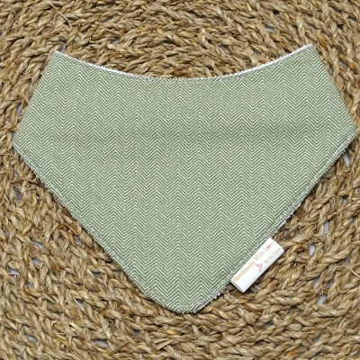 Babete triangular verde com padrão de espinha de peixe e etiqueta Handmade With Love sobre tapete de palha