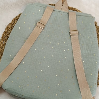 Mochila verde claro com detalhes dourados e alças bege sobre base de fibras naturais
