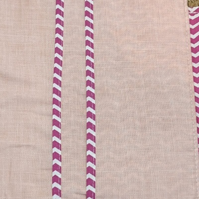 Toalha rosa claro com duas faixas roxas e brancas padrão ziguezague sobre superfície trançada
