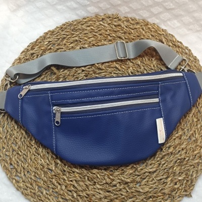 Bolsa pochete azul com zíperes prateados e alça cinzenta sobre base de fibras naturais