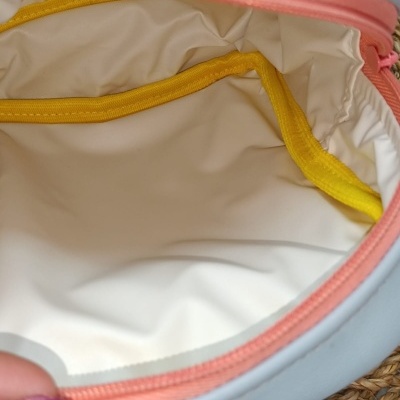 Interior de bolsa branco com bordas amarelas e zíper rosa em fundo de palha