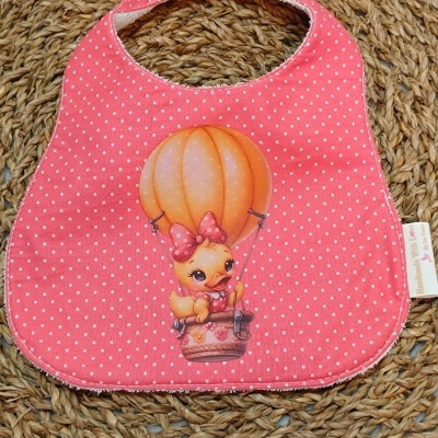Babete cor-de-rosa com bolinhas brancas e desenho de pato em balão de ar quente
