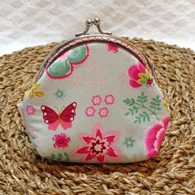 Carteira pequena com padrão floral e borboleta sobre esteira de fibras trançadas