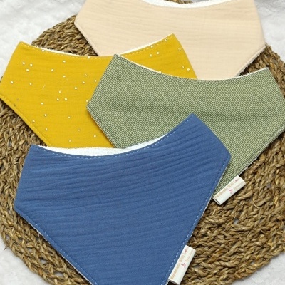 Babetes de tecido em quatro cores diferentes dispostos sobre suporte trançado