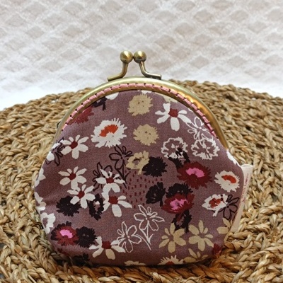 Carteira pequena redonda com tecido floral castanho sobre tapete de ráfia.