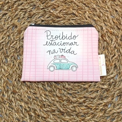 Estojo rosa claro com ilustração de carro e texto, sobre esteira de fibra trançada