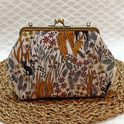 Carteira de tecido floral com fecho metálico dourado sobre centro de mesa trançado.