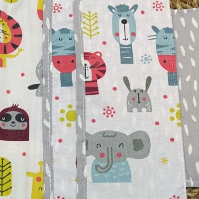 Produto de tecido branco com padrão de animais coloridos e bordas cinza sobre palha