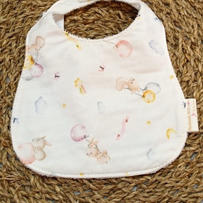 Babete branco com padrão de coelhinhos e balões em fundo de material entrelaçado castanho