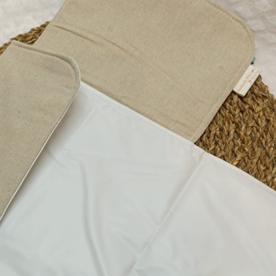 Tapete ou toalha dobrável branco e bege com revestimento impermeável sobre cesto trançado