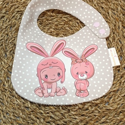 Babete para bebé bege com bolinhas brancas e ilustração de bebé e coelho cor-de-rosa