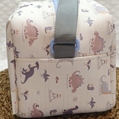 Mala infantil bege claro com padrão de dinossauros coloridos e alça cinza