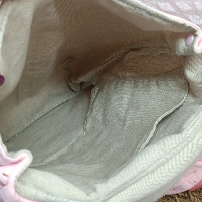 Interior de bolsa de tecido cinzento claro com costuras e botão rosa