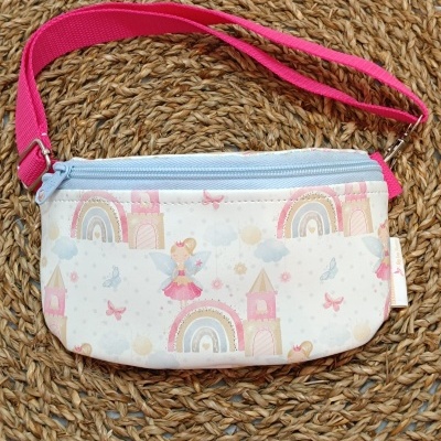 Bolsa infantil branca com padrões de fadas e castelos e alça rosa sobre base trançada castanha