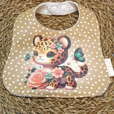 Babete bege com bolinhas brancas e desenho de leopardo com flores e borboletas.