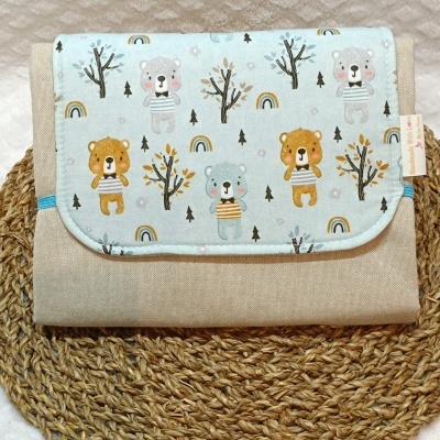 Mala ou necessária de tecido bege com aba azul claro estampada com ursinhos, árvores e arco-íris sobre base de palha trançada