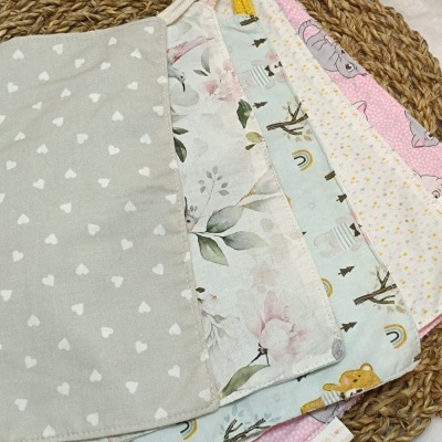 Cinco panos coloridos para bebé com padrões diversos sobre um tapete redondo de fibra natural