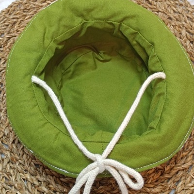 Chapéu verde de tecido com cordão branco sobre superfície de fibra natural entrelaçada