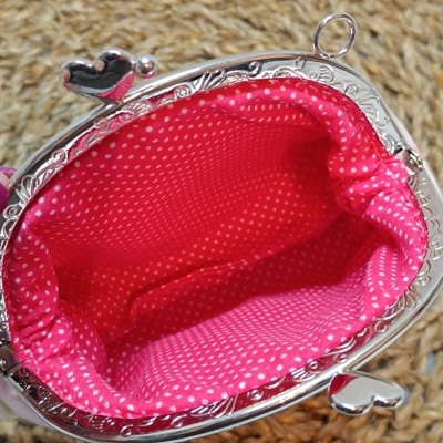 Carteira pequena rosa com fecho metálico em forma de coração e interior com pontos brancos.