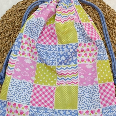 Saco de pano colorido com padrão de quadrados e cordões azuis.