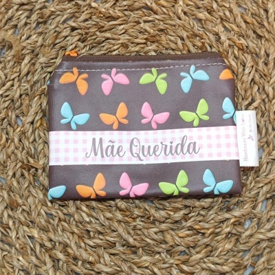 Carteira pequena castanha com borboletas coloridas sobre tapete trançado