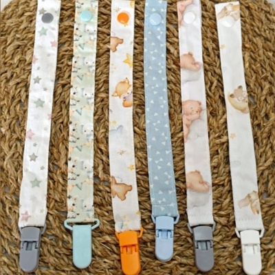 Seis fitas para chucha com diferentes estampas infantis e clips coloridos sobre tapete de fibras naturais