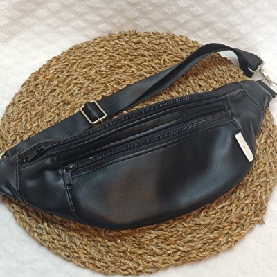 Bolsa pochete preta em material sintético com alça ajustável sobre tapete redondo de fibras