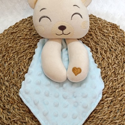 Brinquedo de pelúcia urso bege com tecido azul claro texturizado num tapete trançado