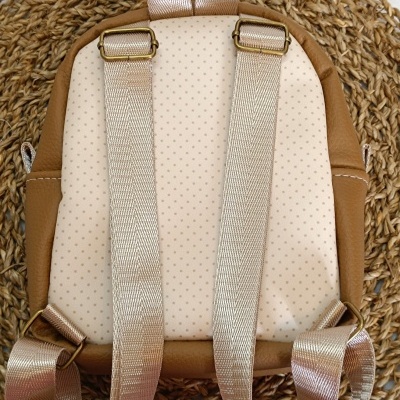 Mochila pequena bege com pontos e pele sintética castanha com alças em fita nylon brilhante.