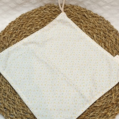 Pano de cozinha branco com pontos coloridos e argola sobre tapete de ráfia