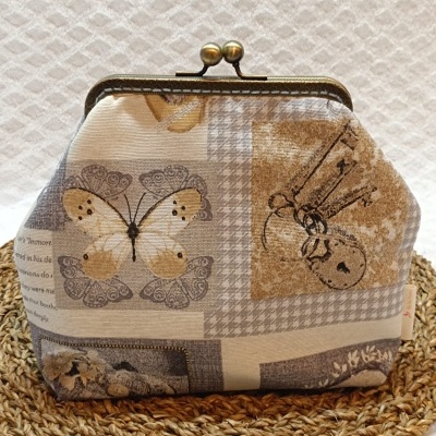 Mala pequena com fecho metálico e padrão vintage com borboleta e chave.