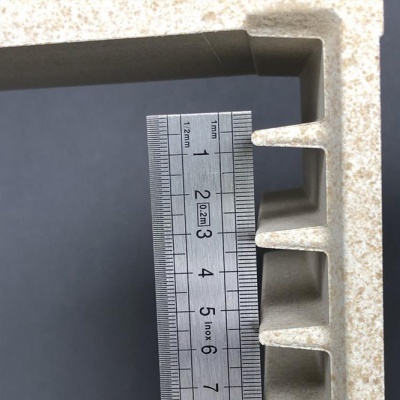 Régua metálica sobre peça bege com ranhuras retangulares e textura granulada