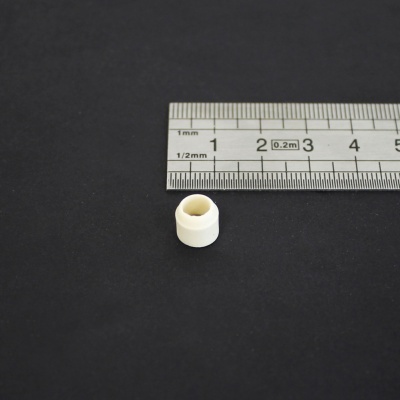 Pequena peça cilíndrica branca em plástico ao lado de régua metálica com marcações.