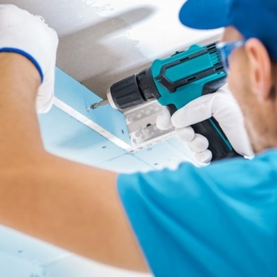 Furadeira eléctrica azul e preta a fixar placa de gesso azul no teto