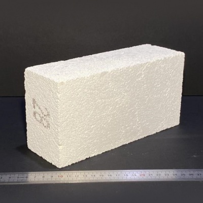 Bloco de construção branco com textura rugosa sobre superfície escura com régua metálica em frente