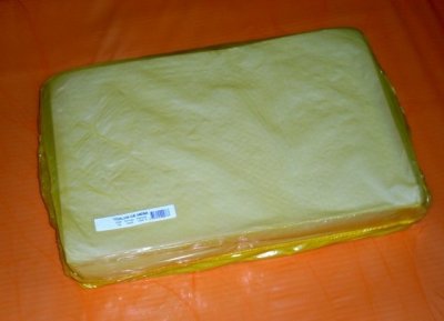 Bloco retangular de queijo embalado em plástico sobre superfície laranja