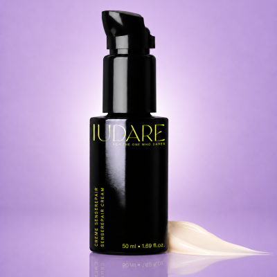 Frasco preto de creme com texto amarelo e creme claro ao lado, fundo lilás.