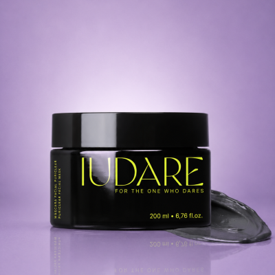Frasco preto de máscara facial Puriclear com texto amarelo sobre superfície lilás.