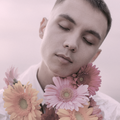 Jovem de olhos fechados com flores gerberas coloridas perto do rosto
